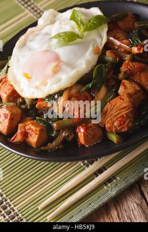 Thai Gai Pad Krapow pollo con basilico, fagioli verdi e un uovo fritto su una piastra di close-up verticale Foto Stock