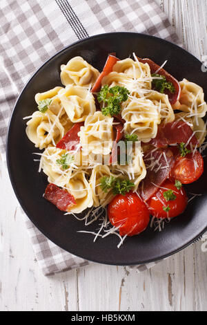 Italian tortellini con prosciutto, pomodori e parmigiano close-up su una piastra. vista verticale da sopra Foto Stock