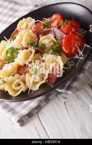 Il cibo italiano: tortellini con prosciutto e formaggio parmigiano close-up su una piastra verticale. Foto Stock