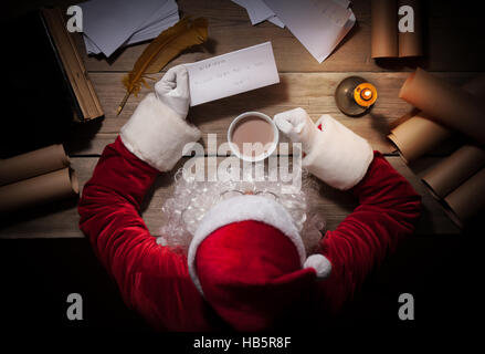 Babbo Natale seduti al tavolo della sua stanza e lettura della lettera di Natale da bambino Foto Stock