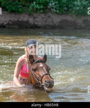 Una giovane donna cavalca il suo cavallo nel fiume Eden a Appleby Horse Fair in Cumbria, Regno Unito Foto Stock