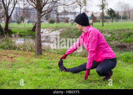 Giovane donna il riscaldamento e lo stiramento delle gambe prima di eseguire in una fredda giornata invernale in un parco. Foto Stock