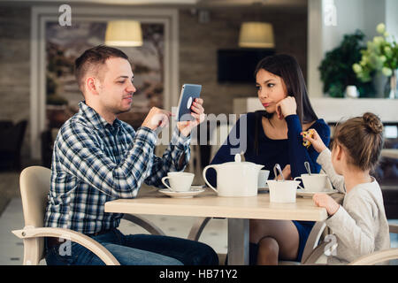 Famiglia moderna valori. Padre addicted circa usando dispositivi elettronici tablet pc, mentre la moglie e la figlia infelice seduti in un caffè Foto Stock