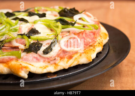 Pizza appena sfornata fatta in casa con peperone verde, basilico, cipolla, salsiccia, prosciutto, mozzarella, pancetta, erbe Foto Stock