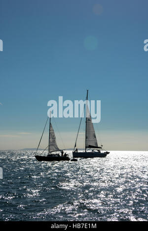 Due yacht ancorati nella baia di tenby prepararsi a salpare su un blu cielo privo di nuvole e il sole riflette sul mare. Foto Stock