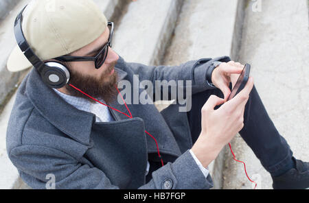 Ragazzo bello ascoltare musica con termofissato in suo cellulare. Foto Stock