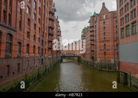 Amburgo, Germania - 18 luglio 2015: il canale della storica Speicherstadt case e ponti a sera con amaising vista del cielo sopra i magazzini, luogo famoso fiume Elba. Foto Stock