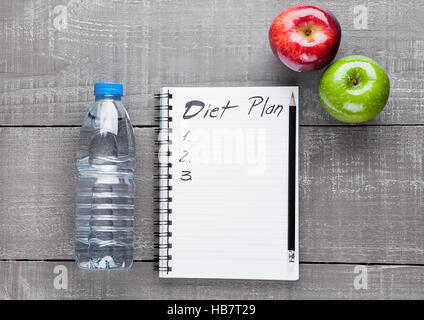 Taccuino di scrittura con mele e acqua come dieta idea sul pannello di legno Foto Stock