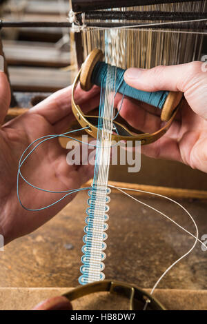 Passementerie maker, mano azienda blue gimp sulla navetta di tessitura che va da sinistra a destra, tessitura crepine o tessuto di confine Foto Stock