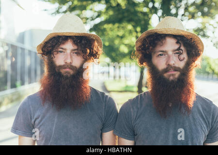 Ritratto di uguali, maschio hipster gemelli indossando cappelli di paglia sul marciapiede Foto Stock