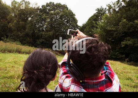 Fratello e Sorella, seduti all'aperto, tenendo selfie, utilizza lo smartphone, vista posteriore Foto Stock