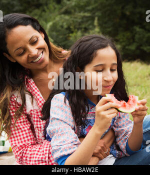 Madre e figlia seduti all'aperto, figlia mangiare anguria Foto Stock