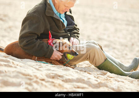 Uomo e cane seduto sulla spiaggia, Constantine Bay, Cornwall, Regno Unito Foto Stock