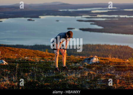 Uomo appoggiato dopo aver eseguito sulla Scogliera al tramonto, Keimiotunturi, Lapponia, Finlandia Foto Stock