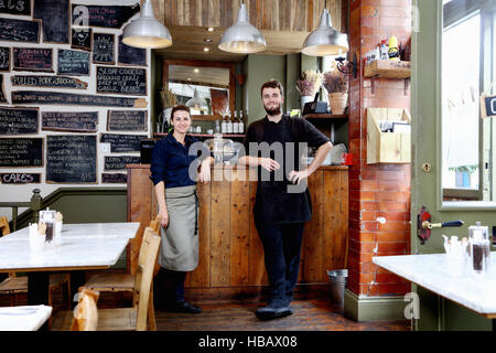Ritratto di maschio e femmina baristi appoggiata sul contatore indipendente di coffee shop Foto Stock