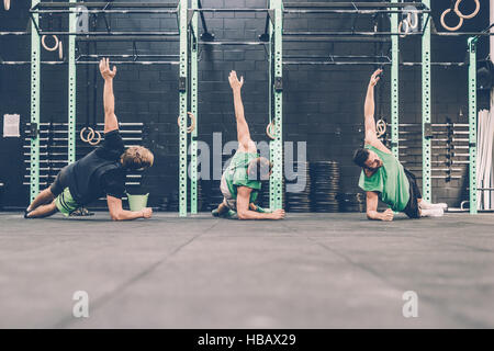Tre maschio cross trainer facendo spinta laterale ups in palestra Foto Stock