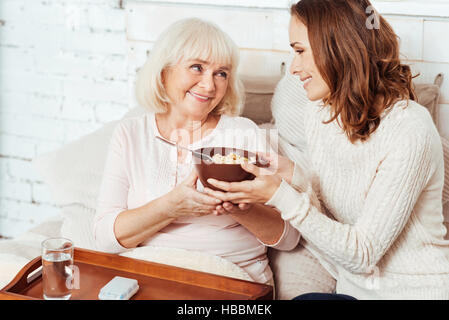 Piacevole donna sorridente dando la prima colazione e la nonna a letto Foto Stock