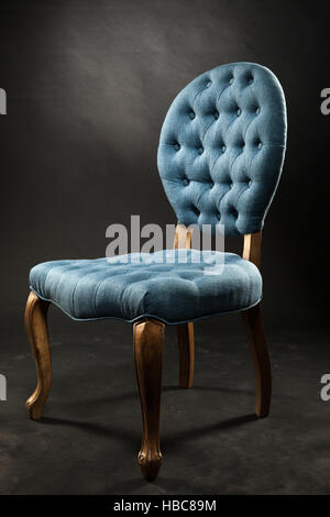 Antica sedia di velluto blu vicino a una stanza buia Foto Stock