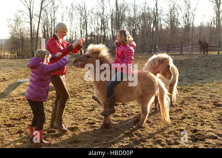 Ragazza giovane cavalcare pony, la madre e la sorella in piedi accanto a loro. Foto Stock