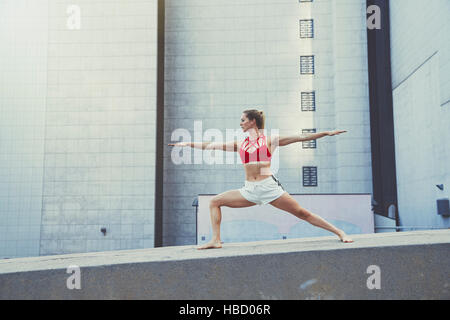 Giovane donna all'aperto, in piedi sulla parete in posizione di yoga Foto Stock