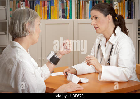 Medico donna spiegare il corretto uso di un polso monitor della pressione del sangue al suo paziente con pressione del sangue alta Foto Stock