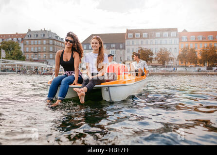 Colpo di giovani sul pedale barca nel lago. Le donne sedute sulla parte anteriore con gli uomini sul retro pedalando la barca. Amici di adolescenti godendo di gite in barca nel lago. Foto Stock