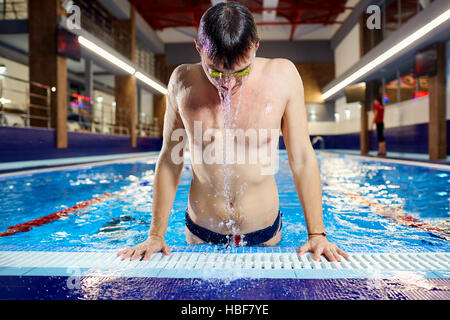 Nuotatore emerge dall'acqua piscina con schizzi in ambienti chiusi. Foto Stock