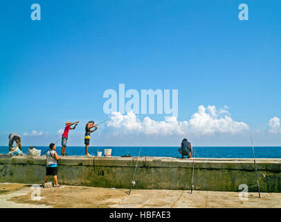 Ragazzi la pesca sul muro del malecón (ufficialmente Avenida de Maceo) un ampio 8 km esplanade, carreggiata e seawall Havana Cuba Foto Stock