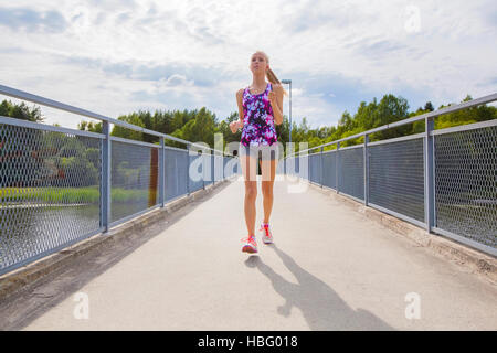 Focalizzato giovane donna in esecuzione sul ponte su un lago Foto Stock