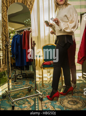 Nessun volto. irriconoscibile persona giovane donna in un rosso tacco alto scarpe guarda nello specchio e scegliere i vestiti Foto Stock