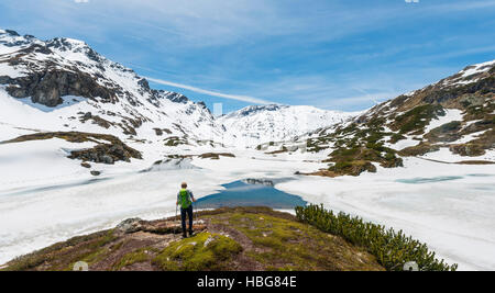 Giovane uomo, escursionista guardando il lago ghiacciato, Unterer Giglachsee, paesaggio di montagna con neve residua, Rohrmoos-Obertal Foto Stock