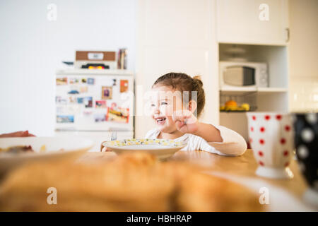 Poco ragazza seduta a tavola a mangiare la prima colazione Foto Stock