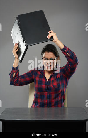 Estremamente mad giovani latino imprenditrice smashing il suo laptop contro la scrivania Foto Stock