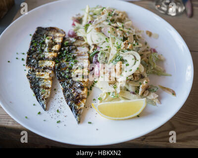 Sgombri filetti di pesce servito con insalata con mele e noci. Su una piastra bianca su una tavola di legno con una fettina di limone. Foto Stock