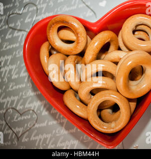 Vista Тop. Bagel vetrata sulla targhetta rossa a forma di cuore su grigio parole scarabocchiati sfondo. Foto Stock