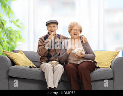 Senior gioiosa giovane seduto su un divano e mangiare popcorn Foto Stock