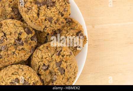 Top vedere da vicino alcuni dei fiocchi d'avena i biscotti al cioccolato su una piastra bianca in cima a una tavola di legno. Foto Stock