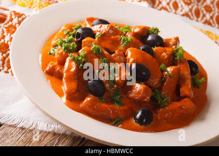 Spezzatino di maiale in salsa piccante di vino, pomodori e crema con olive nere close-up su una piastra. Posizione orizzontale Foto Stock