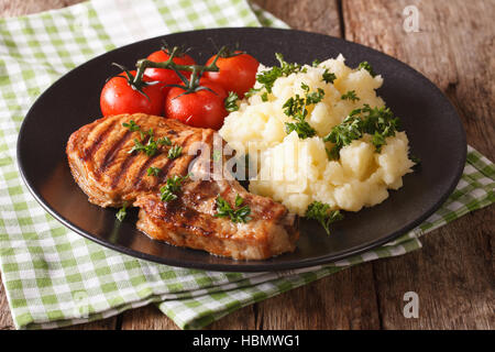 Carne di maiale alla griglia T-bone steak guarnita con purè di patate e pomodoro close-up su una piastra orizzontale. Foto Stock