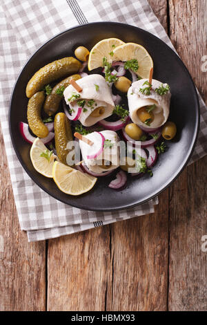 Rotoli di aringhe marinate con olive, cipolla, sottaceti e limone close-up su una piastra sul tavolo. vista verticale da sopra Foto Stock