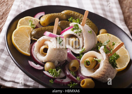 Rotoli di aringhe marinate con olive, cipolla, sottaceti e limone close-up su una piastra sul tavolo. Posizione orizzontale Foto Stock