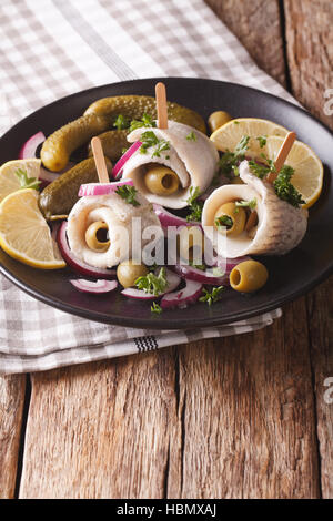 Rotoli di aringhe marinate con olive, cipolla, sottaceti e limone close-up su una piastra sul piano verticale. Foto Stock