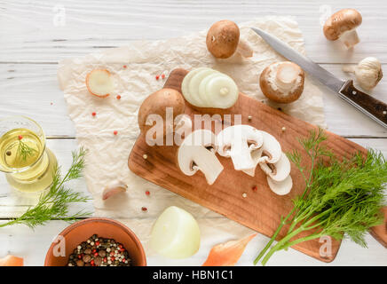 Marrone di funghi champignon su un tagliere. Bianco scrivania in legno erbe e cipolle. Foto Stock