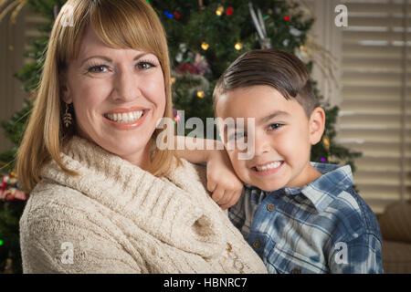 Felice madre e razza mista figlio abbraccio vicino al loro albero di Natale. Foto Stock