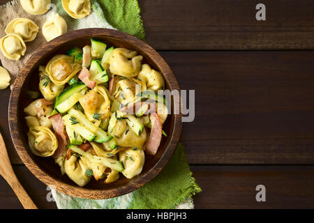 Formaggio cotto al forno tortellini o pulsante di emergenza la pasta con le zucchine, pancetta e timo in ciotola di legno, fotografato overhead sul legno scuro con luce naturale Foto Stock