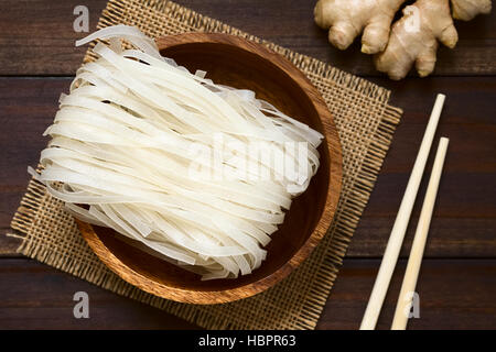 Materie di farina di riso tagliatelle in ciotola di legno, fotografato overhead sul legno scuro con luce naturale (messa a fuoco selettiva) Foto Stock