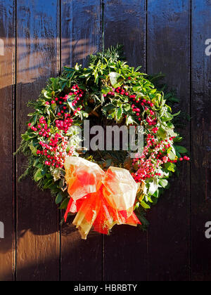 Natale agrifoglio ghirlanda pendente da un marrone di legno verniciato porta. Foto Stock