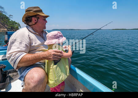 Un nonno aiuta i suoi nipoti a pescare su una barca. Foto Stock