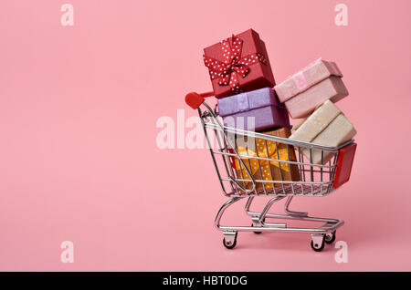 Un carrello pieno di doni di diversi colori su un sfondo rosa, con lo spazio negativo Foto Stock