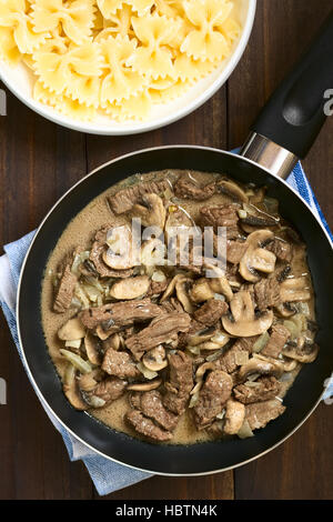 Carni bovine Stroganoff in padella, un piatto fatto di pezzi di carne di manzo, funghi e cipolla in salsa di panna con la pasta sul lato Foto Stock